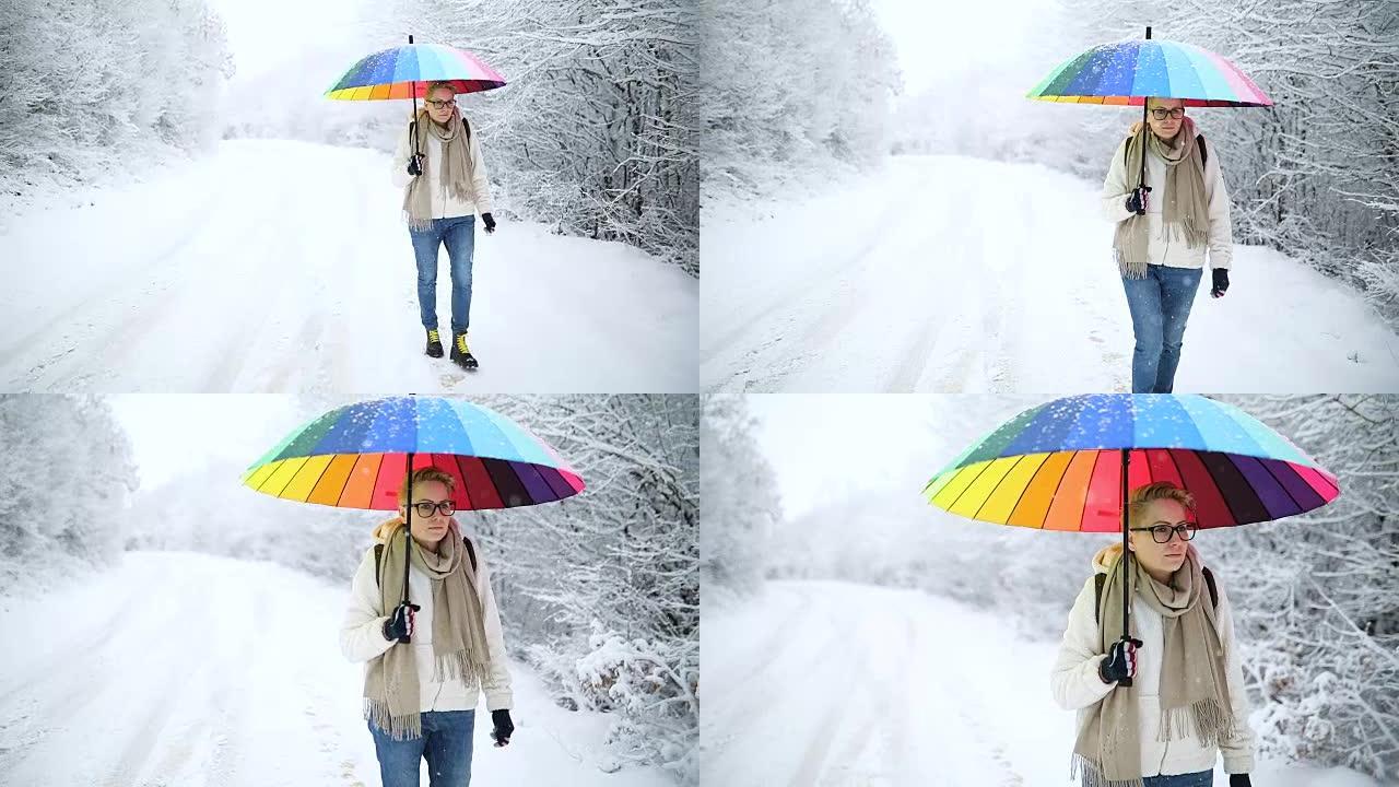在冬季大自然中散步的年轻女孩拿着彩虹伞