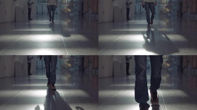 穿着牛仔裤的男人们沿着人工照明的走廊走向摄像机
