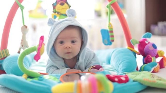 可爱的男婴在五颜六色的健身房，在家里玩悬挂玩具，婴儿活动和婴儿早期发育的游戏中心。孩子们在家玩耍