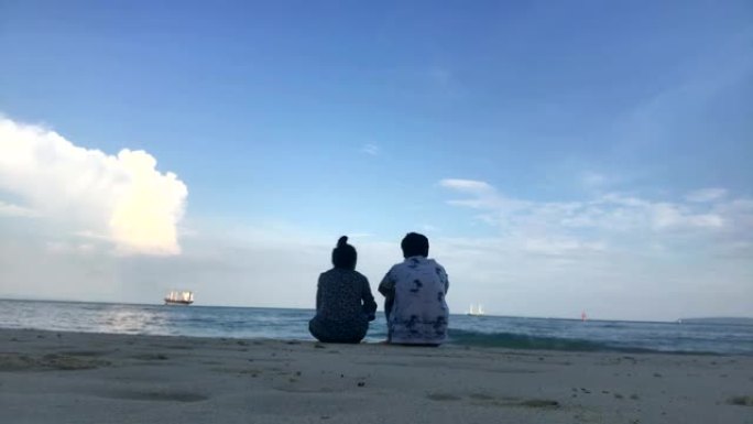 年轻浪漫的夫妇坐在海滩上欣赏美丽的景色