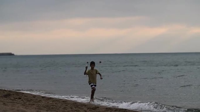 梦想家男孩在傍晚带着纸飞机在美丽的天空中沿着海岸奔跑