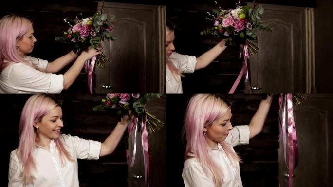 一个粉红色头发的女孩在她面前手里拿着各种各样的花。花束装饰着悬挂的丝绸丝带。侧视图