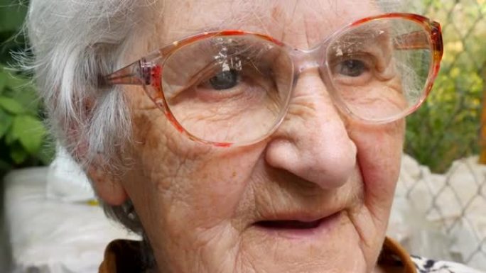 戴眼镜的老妇人向前看，面带微笑。戴眼镜的快乐奶奶在户外的肖像。祖母的情感。关闭慢动作