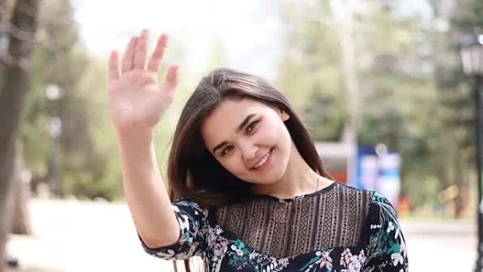 20岁快乐的年轻女人向相机挥手告别或问好。欢迎观众的女孩