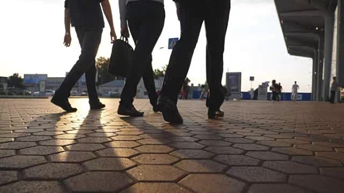 三个商人的脚在机场附近行走，背景是太阳耀斑。面目全非的商人一起去终点站。自信的人正在去上班的路上。同