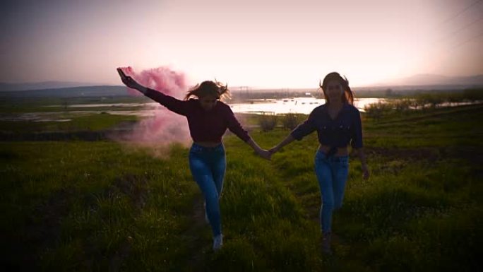 两名年轻女子奔跑并旋转着粉红色的烟雾弹，慢动作
