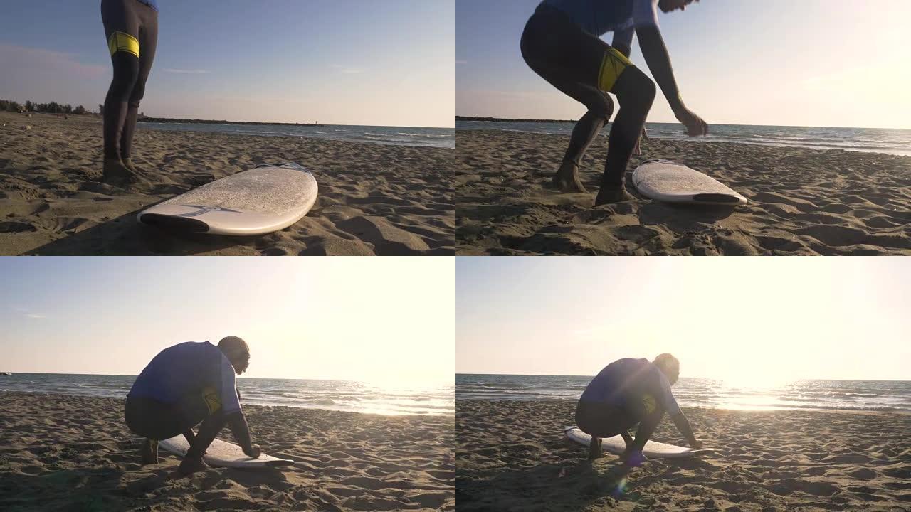 身穿潜水衣的年轻人在日落时在沙滩上冲浪板上擦面漆蜡，准备