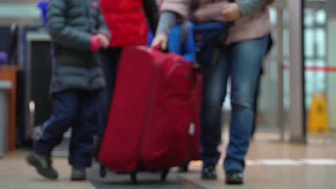 机场安检入口行李控制。扫描行李。带有大型红色行李箱的家庭通过入口控制装置，并将行李装载到手推车上
