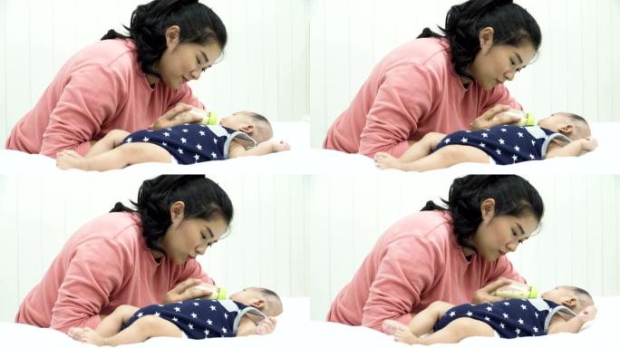 侧视图: 她的婴儿躺在白色床上时从奶瓶中喝牛奶