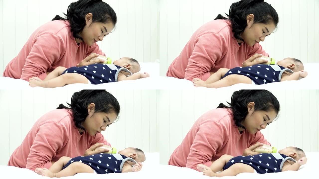 侧视图: 她的婴儿躺在白色床上时从奶瓶中喝牛奶