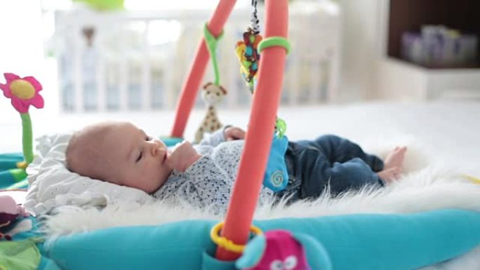 可爱的男婴在五颜六色的健身房，在家里玩悬挂玩具，婴儿活动和婴儿早期发育的游戏中心。孩子们在家玩耍
