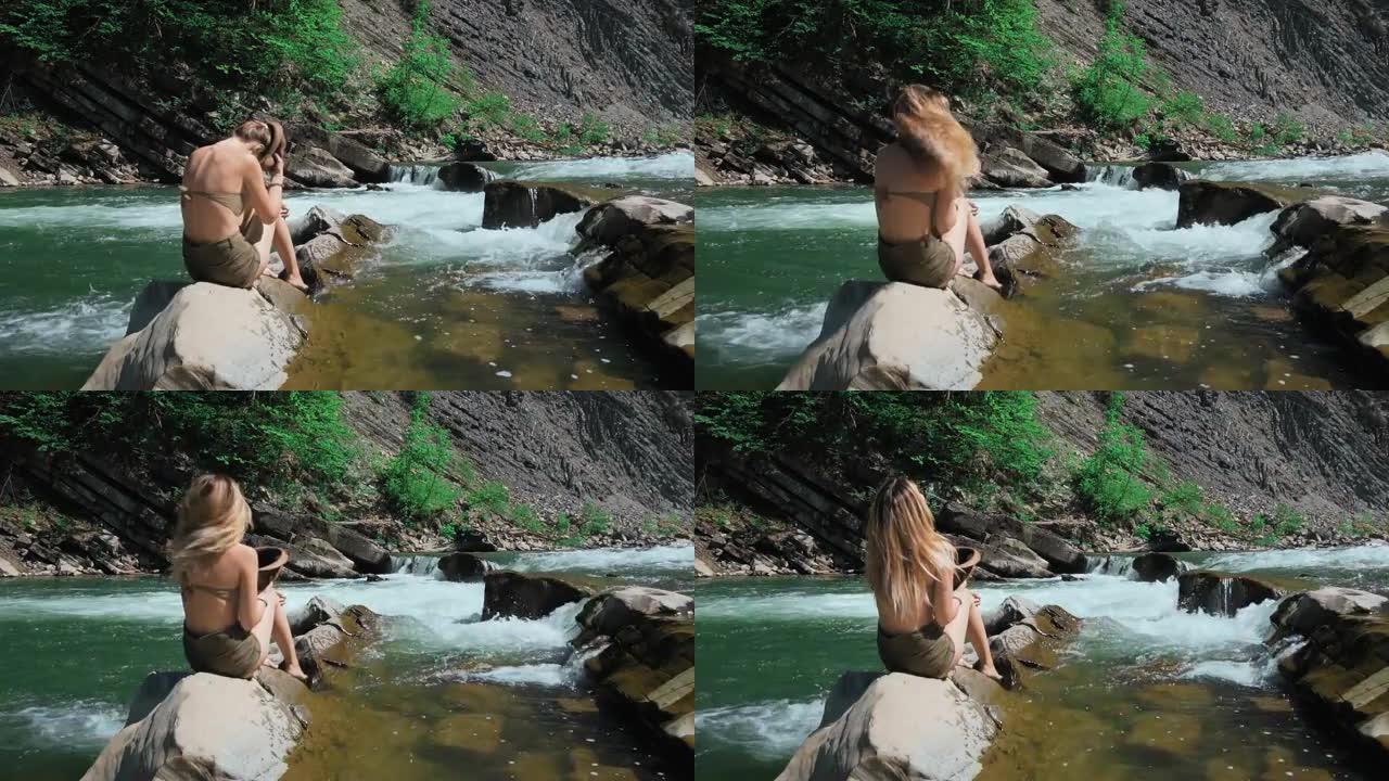 年轻女子坐在瑞士山河岸边的岩石上。脱下帽子，张开长发。自由和纯洁的概念，快乐。卸掉枷锁。慢动作