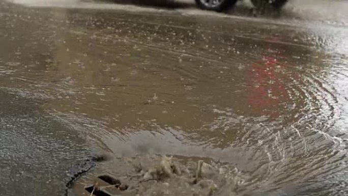 雨水落在道路上，流经下水道。汽车在洪水泛滥的道路上行驶。