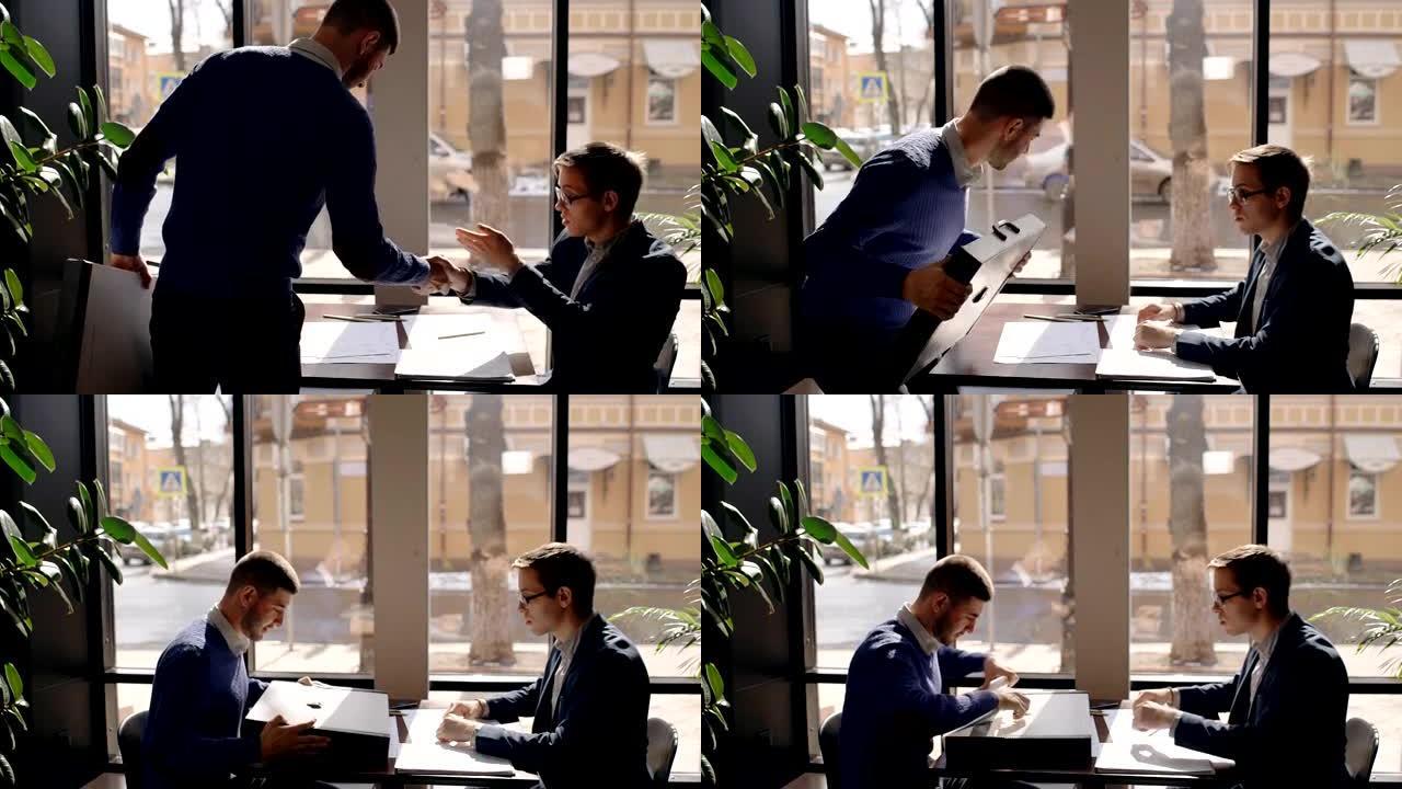 两个男性商业伙伴在咖啡馆见面，打招呼，打招呼，握手，坐在桌子旁讨论新项目，男人打开公文包，拿出文件