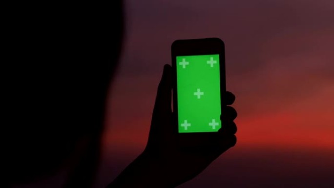 剪影女人的黄昏时间使用智能手机的色度键拍摄城市景观
