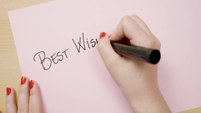 女性用黑色记号笔在粉红色纸上用大写字母写下最美好的祝愿