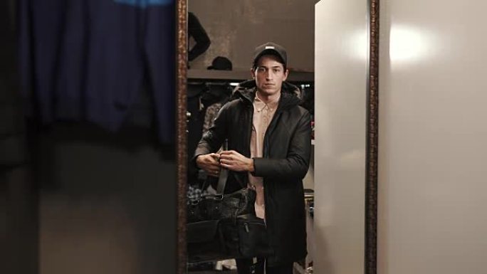 时髦的家伙正在用商店的镜子里的大包，外套和帽子来估计自己的形象