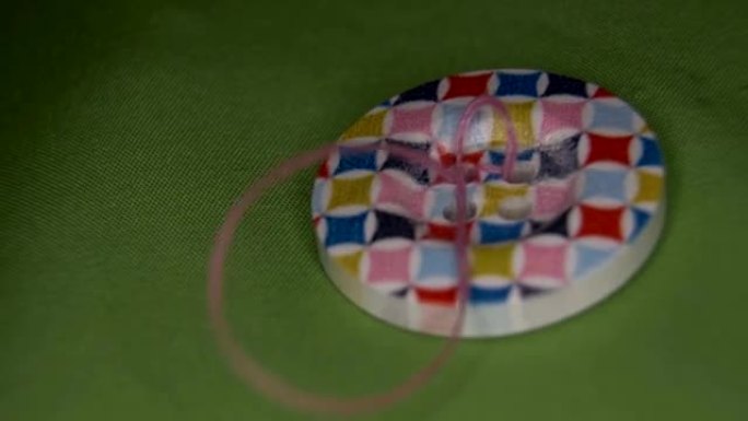 在绿色织物上缝制彩色纽扣，用粉红色的线，特写