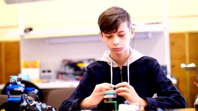12岁的男孩，从立方体，盘子，电路，电线在设计师中扮演角色。一个小发明家从设计师的不同部分创建机器人