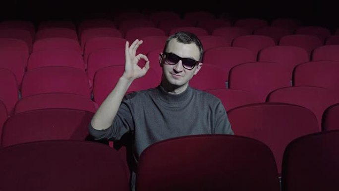 单身男子坐在黑暗电影院舒适的红色椅子上，并显示ok标志