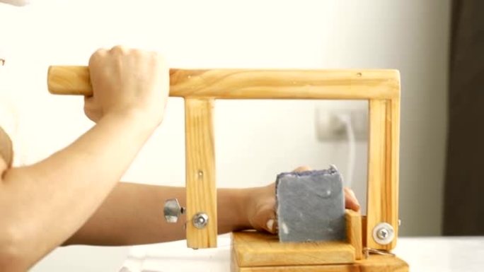 亚洲女性的小企业正在用切割过程制作有机肥皂，同时使用硬木面包肥皂刀具手工精密切割肥皂在她的房间修剪她