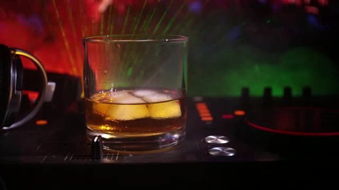 夜总会dj控制器上的玻璃和带冰块的威士忌。Dj耳机在夜总会的音乐派对上戴一杯whilsky，配有迪斯