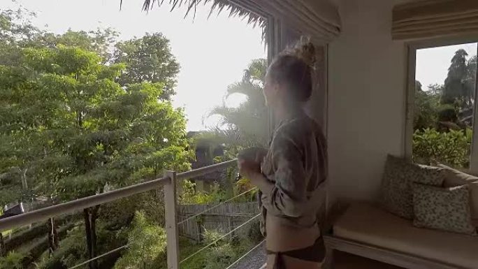年轻女子在雨林上方的豪华树屋里喝茶，看着风景，早晨放松自然和热带气候的概念。人们享受生活幸福的另类生
