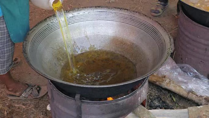 Woman pouring fried oil into a large outdoor wok c