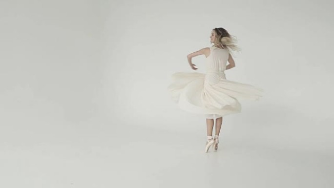 美丽、清新和青春的概念。芭蕾舞女演员穿着白色背景上的轻盈连衣裙旋转。慢动作