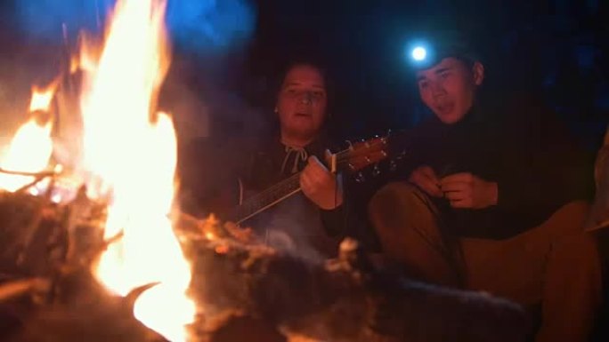 年轻朋友在夜晚的树林篝火旁唱歌和弹吉他