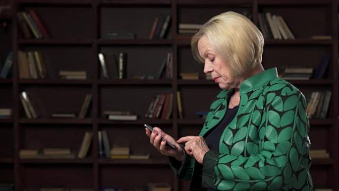 严肃的老年妇女在图书馆使用智能手机