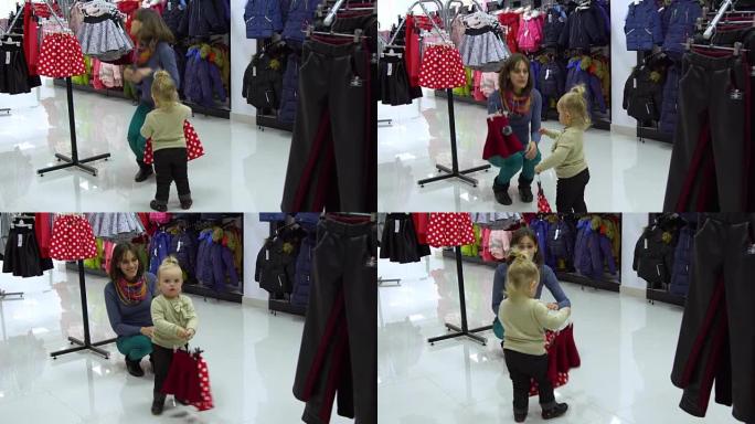 一个可爱的小女孩和她的母亲在精品店里选择童装。妈妈和孩子在商店里挑选衣服。考虑儿童裙子。