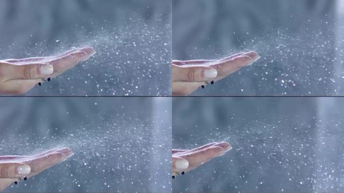 许多银色闪光从灰色背景上的女人的手上掉下来。慢动作。