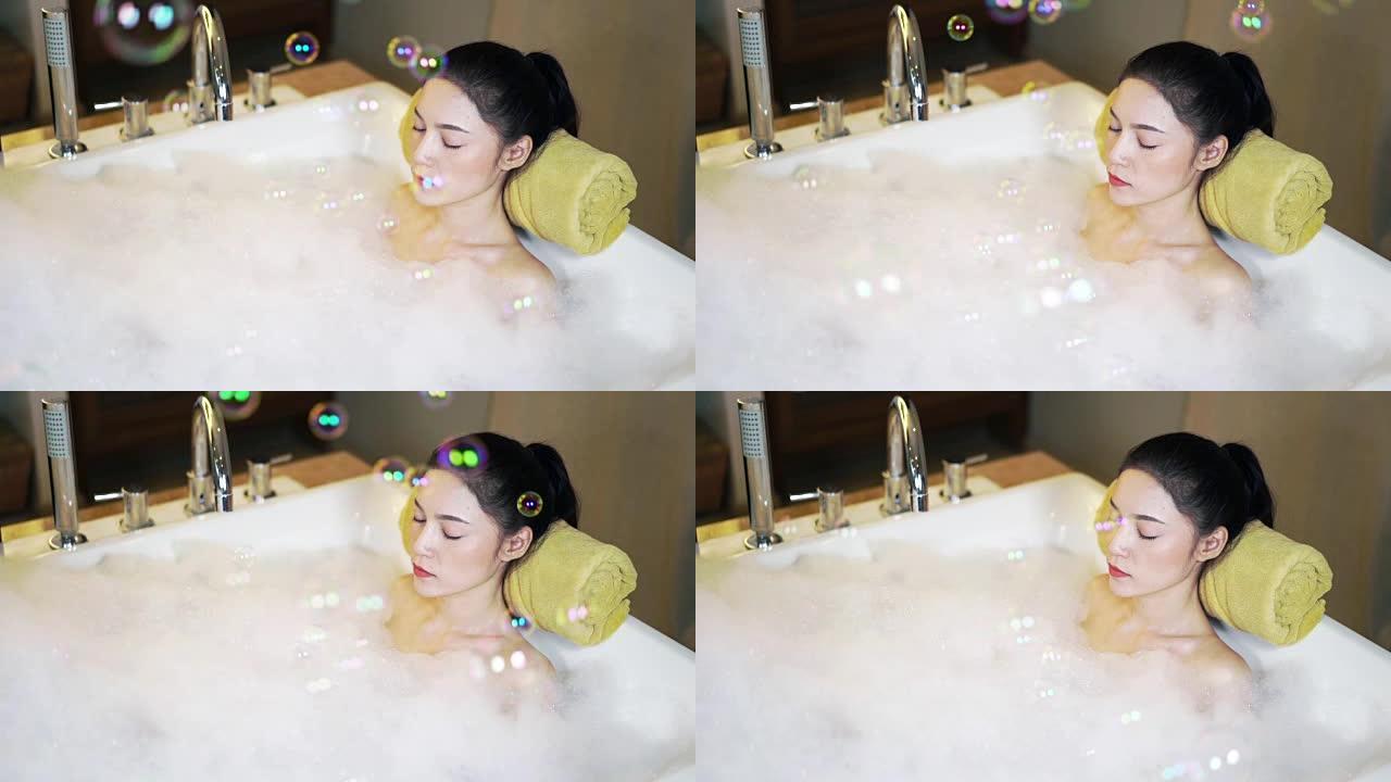 女人的慢动作在浴缸中闭上眼睛放松，气泡漂浮