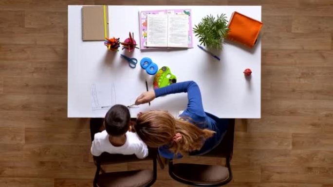 年轻的母亲和儿子一起画画，坐在桌子后面，孩子在做作业顶层拼花木地板