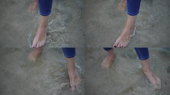 女性赤脚站立并在背景沙质底部移动海水