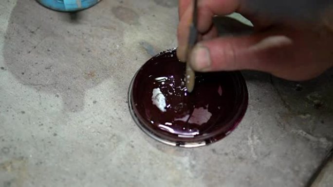 工匠的手将木棍浸入油漆中继续绘画