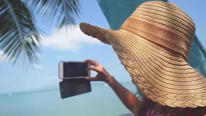 美丽的年轻女子戴着墨镜和帽子微笑着在海滩上拍照暑假慢动作。1920x1080
