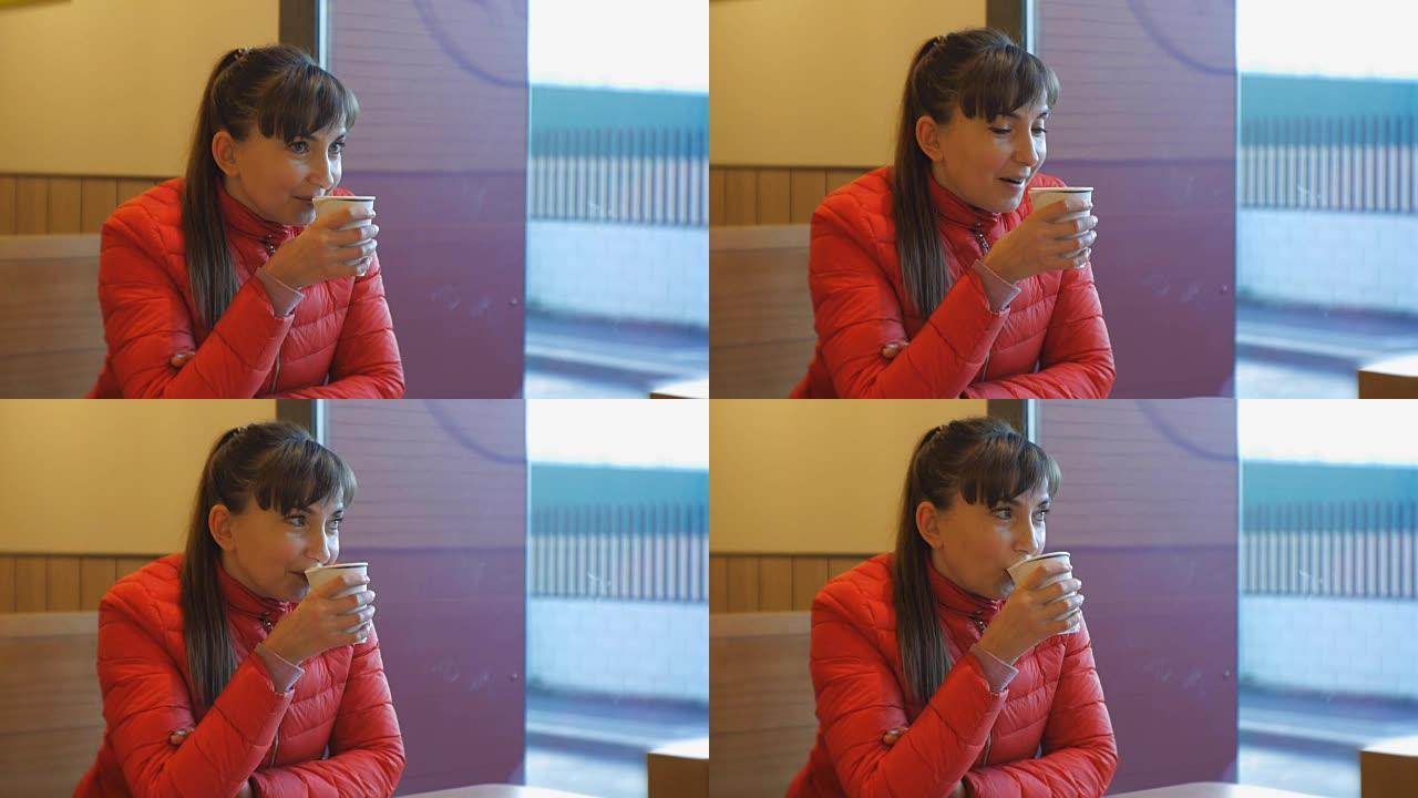 迷人的女人在咖啡馆喝咖啡。穿着红色泡泡夹克的高加索女性肖像，享受着咖啡香味，在窗户附近啜饮卡布奇诺咖