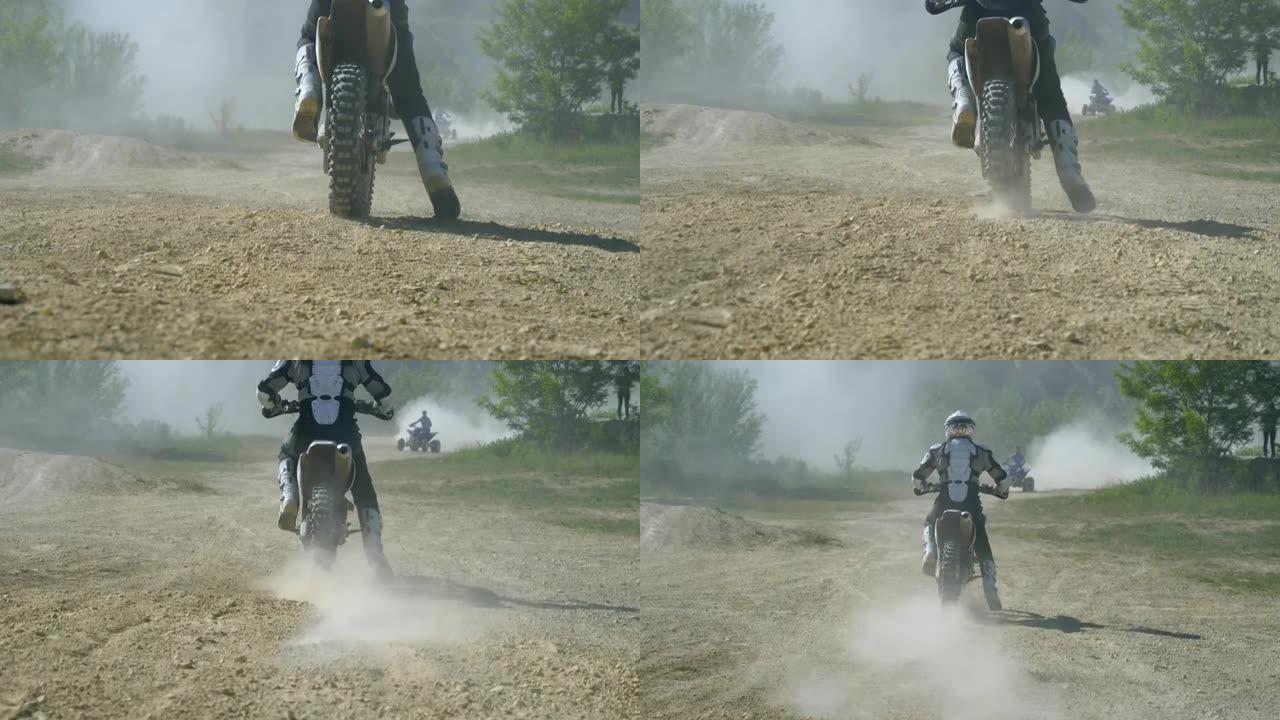 越野摩托车手骑着他的越野摩托车，扬起尘土。后视图慢动作低角度视图近