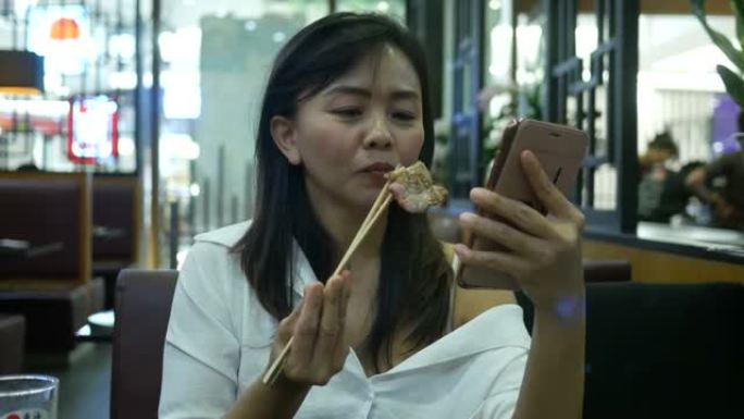 女人用筷子吃烧烤猪肉并使用网络摄像头