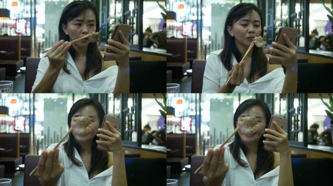 女人用筷子吃烧烤猪肉并使用网络摄像头