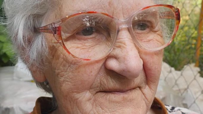 戴眼镜的老妇人向前看，面带微笑。戴眼镜的快乐奶奶在户外的肖像。祖母的情感。关闭慢动作