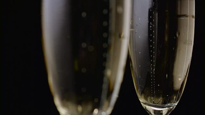 两杯香槟泡泡特写升起。黑色背景