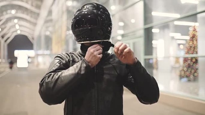 年轻有魅力的摩托车手，戴着头盔和定制摩托车在夜街上