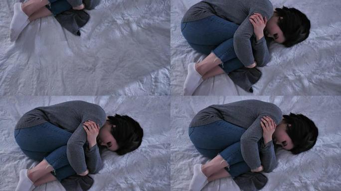 镜头多莉，顶拍年轻悲伤的亚洲女孩躺在床上，用胳膊抱着膝盖，不开心，白色卧室50 fps