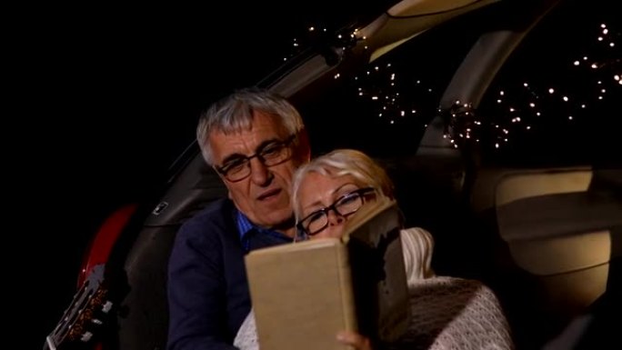 高级夫妇坐在敞开的汽车后备箱里看书