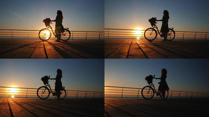 年轻迷人的女人穿着复古自行车的剪影，在日出或日落时在海边的木堤上行走。浪漫旅行理念。4k