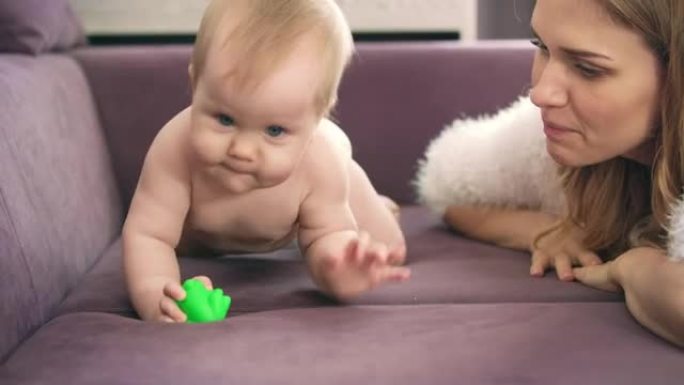 可爱的婴儿爬在紫罗兰的床上。赤裸的孩子在尿布啃玩具