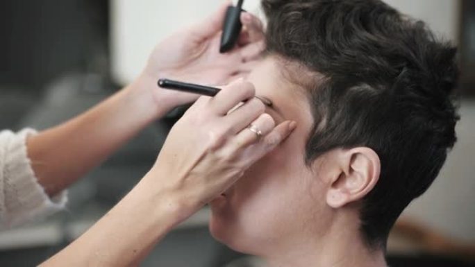 化妆师的手的特写视图用刷子为中年模特画眉毛，短发假睫毛。慢动作镜头